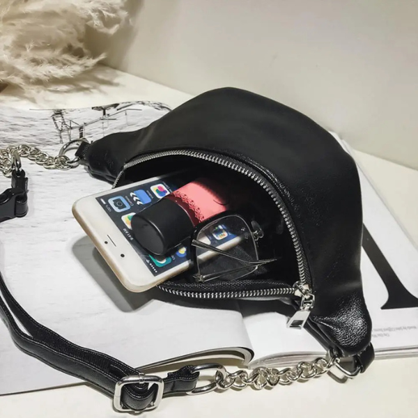 Sac banane femme cuir noir posé sur un livre, équipé d’une chaîne et d’une fermeture éclair
